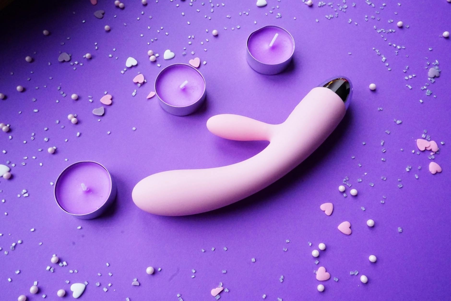 Close-up of a hand holding an orange vibrator against a minimalistic purple backdrop